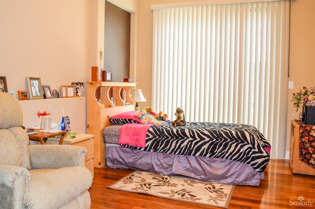A cozy bedroom with a zebra print blanket, stuffed animals on the bed, and vertical blinds allowing natural light to enter.