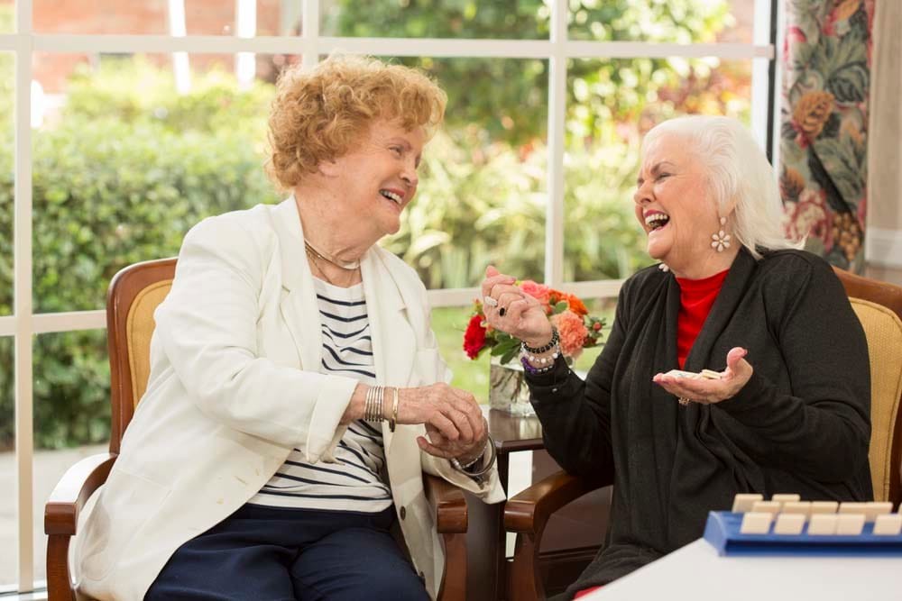 Two elderly women laughing and enjoying a conversation indoors.