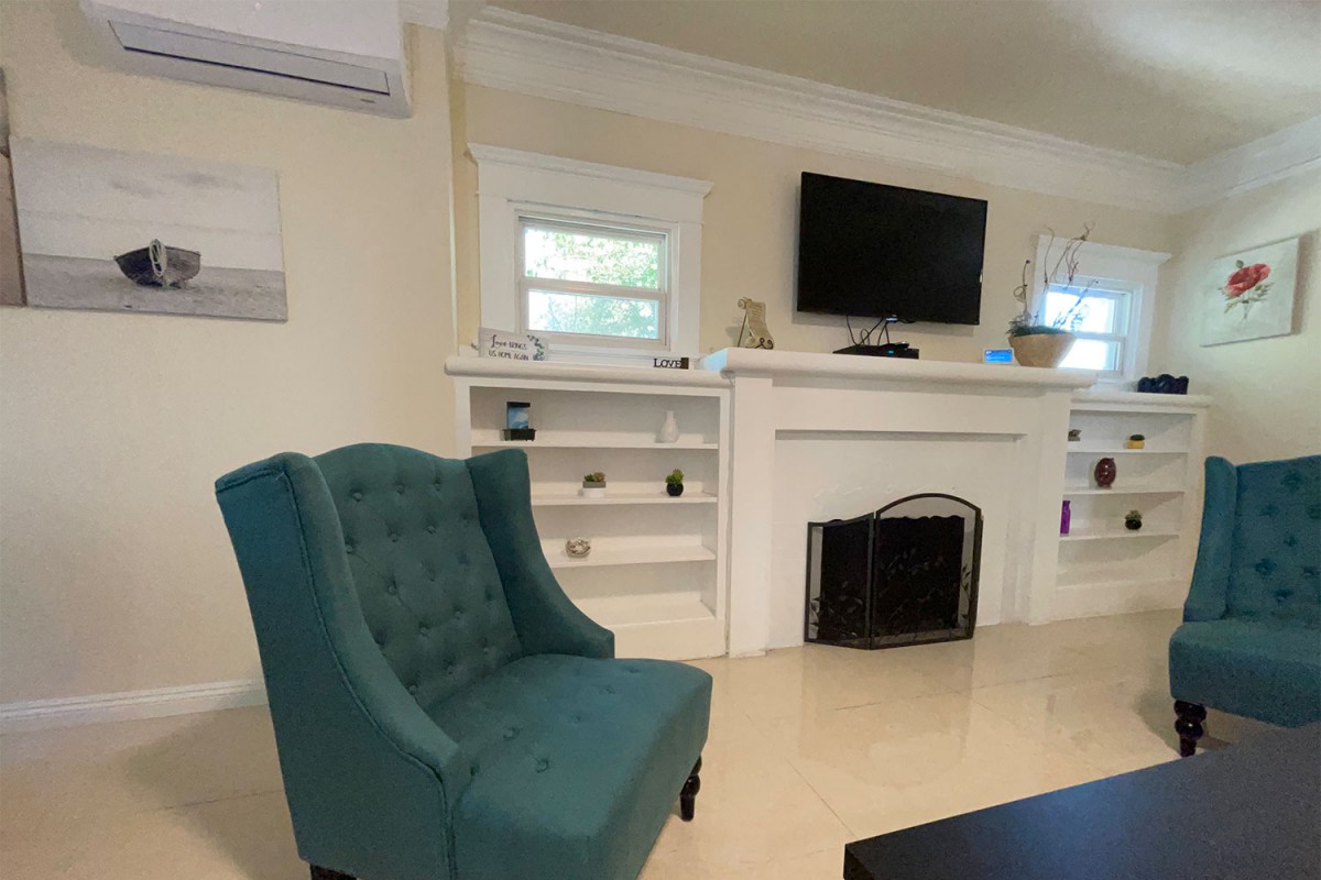 A cozy living room featuring a teal armchair, a fireplace with a TV mounted above, and built-in shelves.