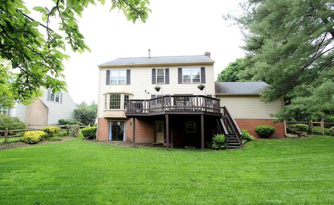 A two-story house with a wooden deck overlooking a spacious backyard.