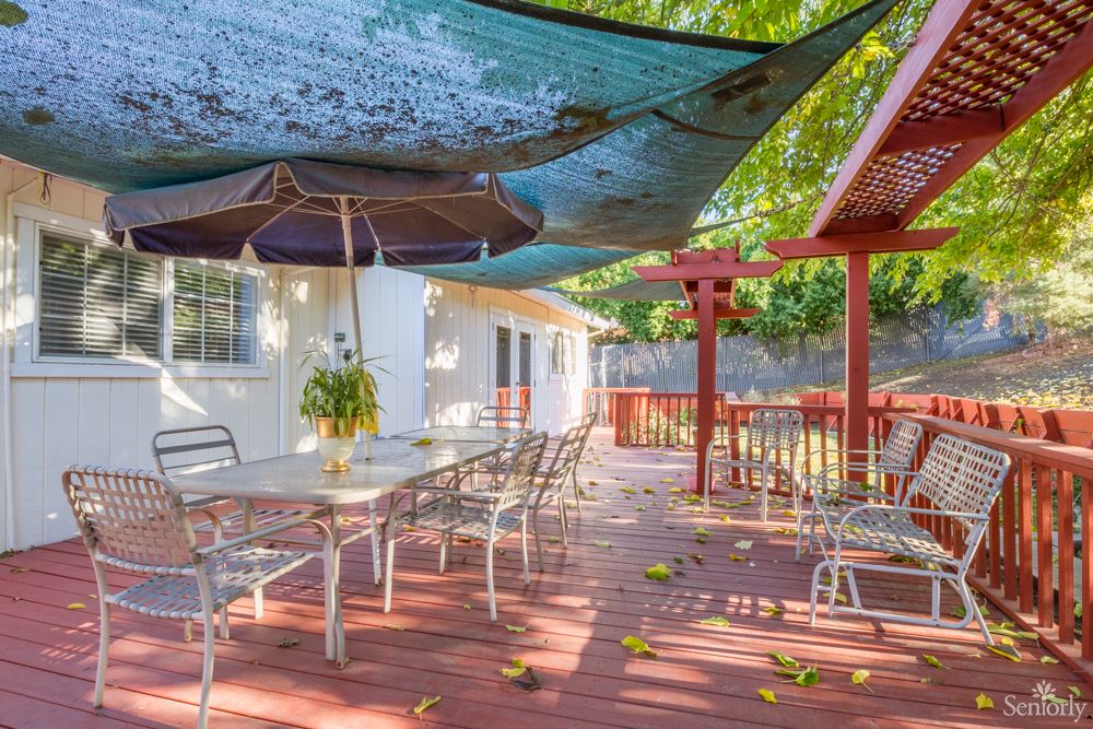 A sunny outdoor patio with a deck, featuring chairs and table under shade sails.
