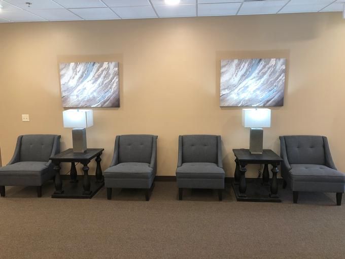 A waiting room with several chairs and lamps arranged neatly along the wall, featuring abstract artwork.