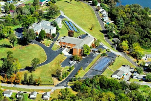 Aerial view of a complex featuring buildings, roads, and solar panels surrounded by greenery.
