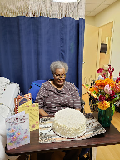 A joyful celebration with an elderly woman surrounded by a cake, flowers, and greeting cards.