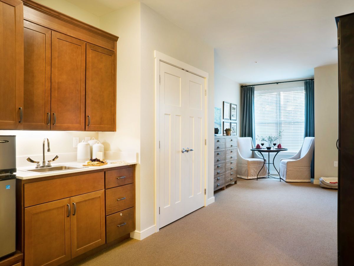 A cozy apartment interior with a small kitchen and a bright living area with seating by the window.