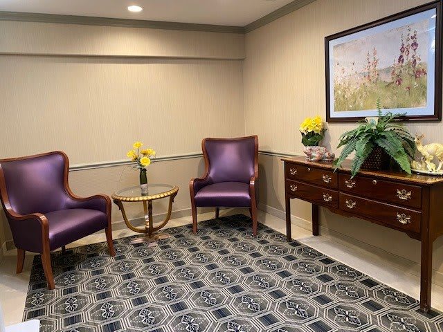 A cozy waiting room with purple chairs, a small glass table, and decorative elements like flowers and artwork.