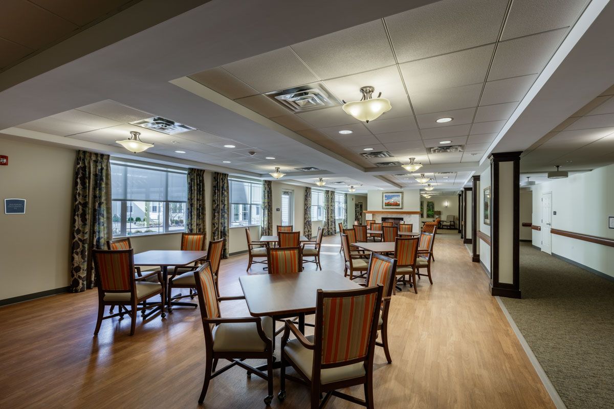 A spacious dining area with neatly arranged tables and chairs, featuring overhead lighting and large windows.