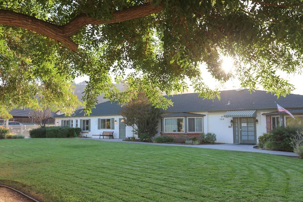 A sunny view of a suburban house with a well-maintained lawn and trees.
