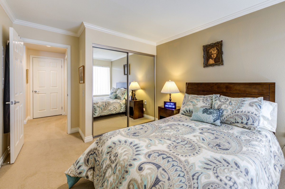 A cozy bedroom featuring a bed with patterned bedding, mirrored closet doors, and stylish decor.