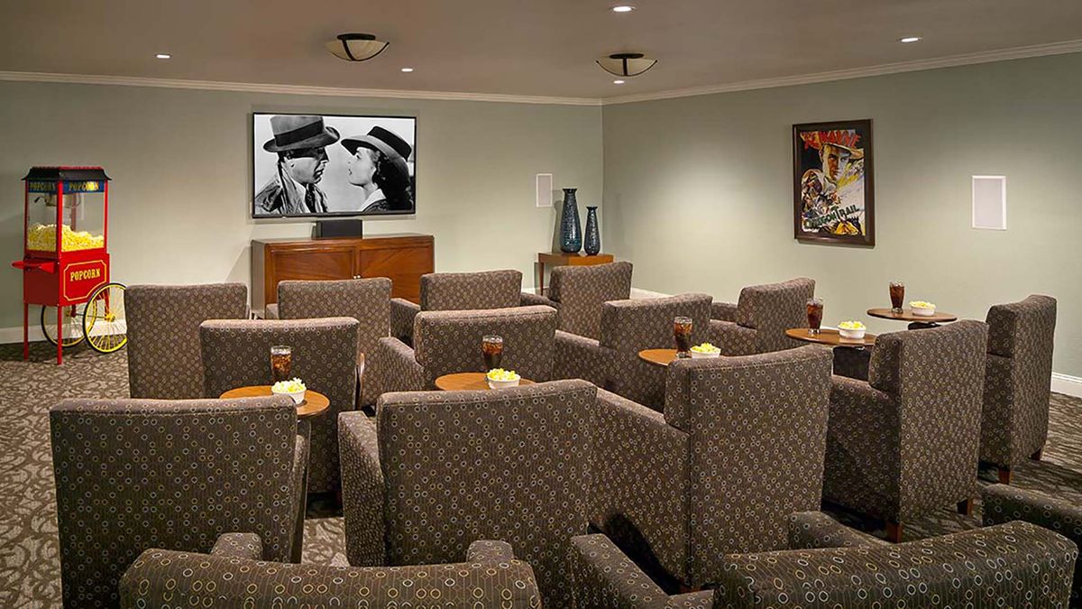 A small, cozy movie theater with multiple rows of comfortable seating and a screen displaying a black-and-white film.