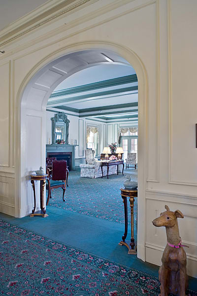A classic, elegantly decorated room with a view through an archway, showcasing period furniture and a large fireplace.