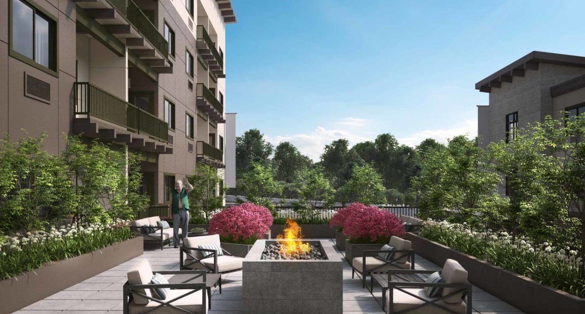 A modern apartment complex with an outdoor seating area featuring a fire pit and lush landscaping.