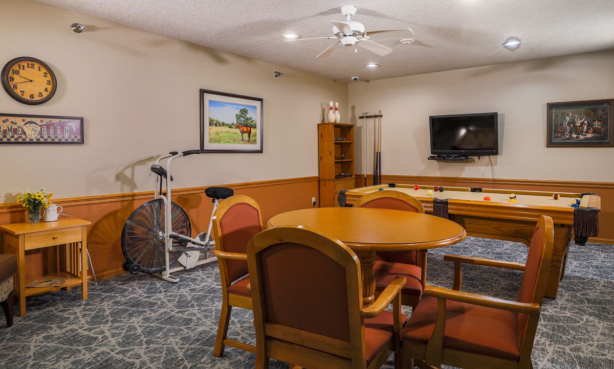 A cozy meeting room featuring a round table with chairs, a wall-mounted television, an exercise bike, and a decorative painting.