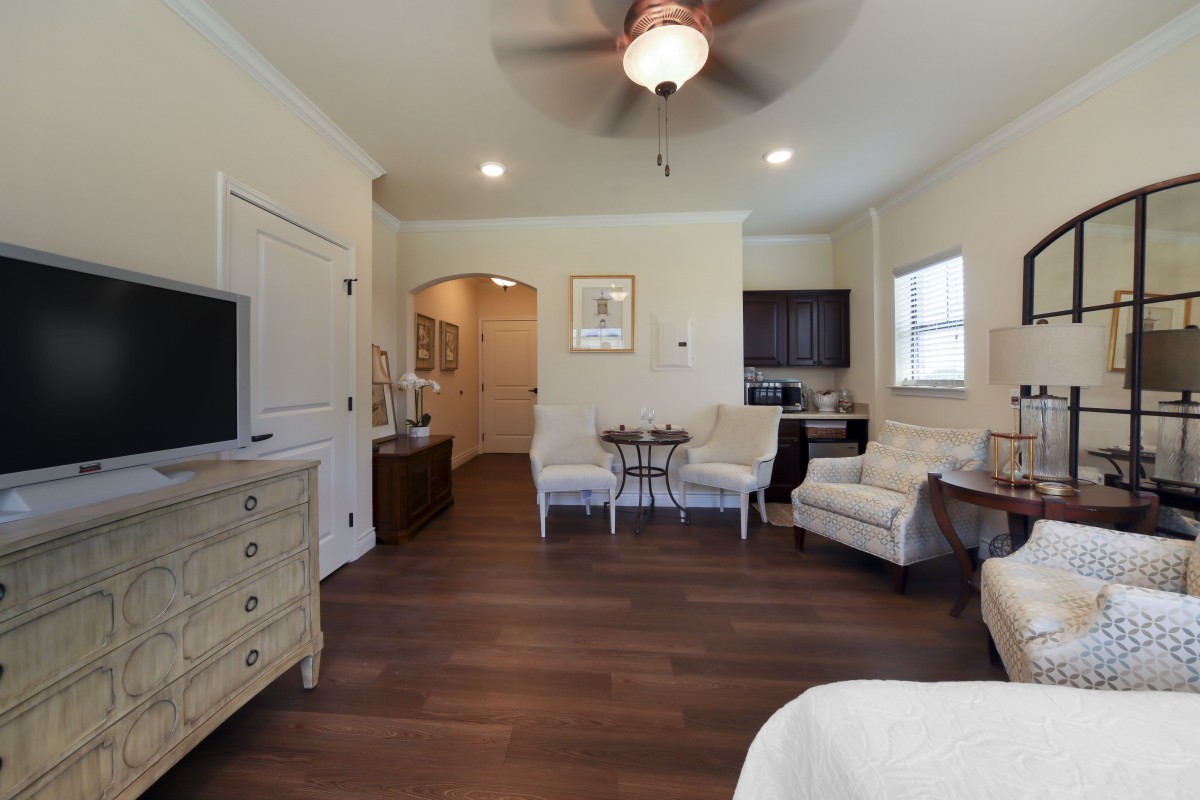 A cozy living room with wooden flooring, featuring comfortable chairs, a ceiling fan, and tasteful home decor.