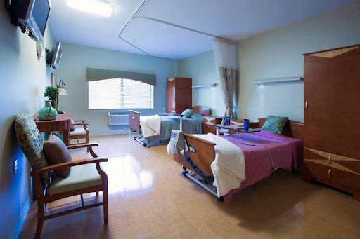 A well-lit and clean hospital patient room featuring two beds and seating.