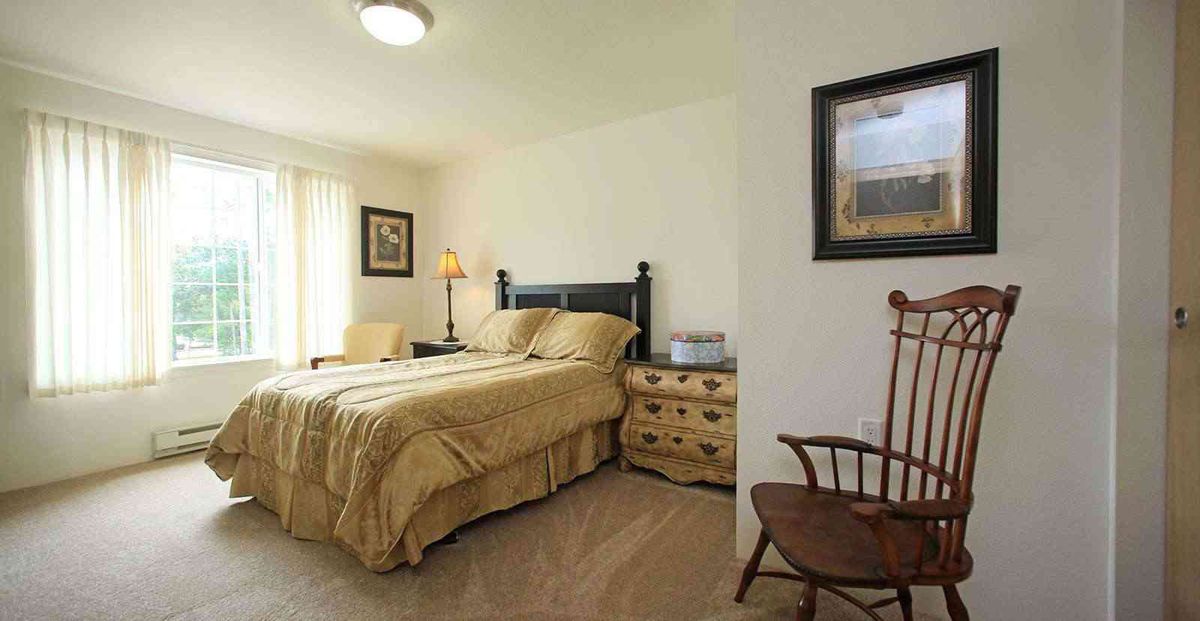 A cozy bedroom with a double bed, bedside table, and a wooden chair.