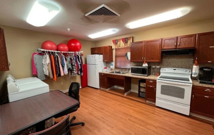 A multi-purpose room featuring a kitchen area, clothes rack with hanging garments, and exercise balls.