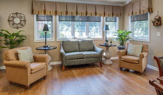 A cozy living room with a sofa, armchairs, and large windows providing natural light.