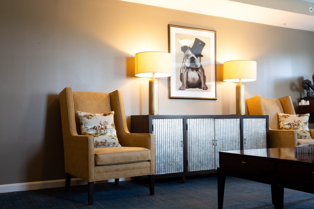 A cozy living room featuring a comfortable armchair, decorative lamps, and a humorous artwork of a dog in a top hat.