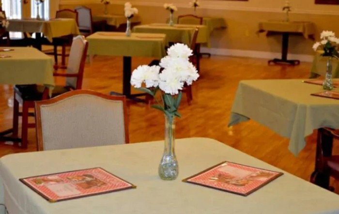 A restaurant table with white flowers in a vase and menus placed on it.