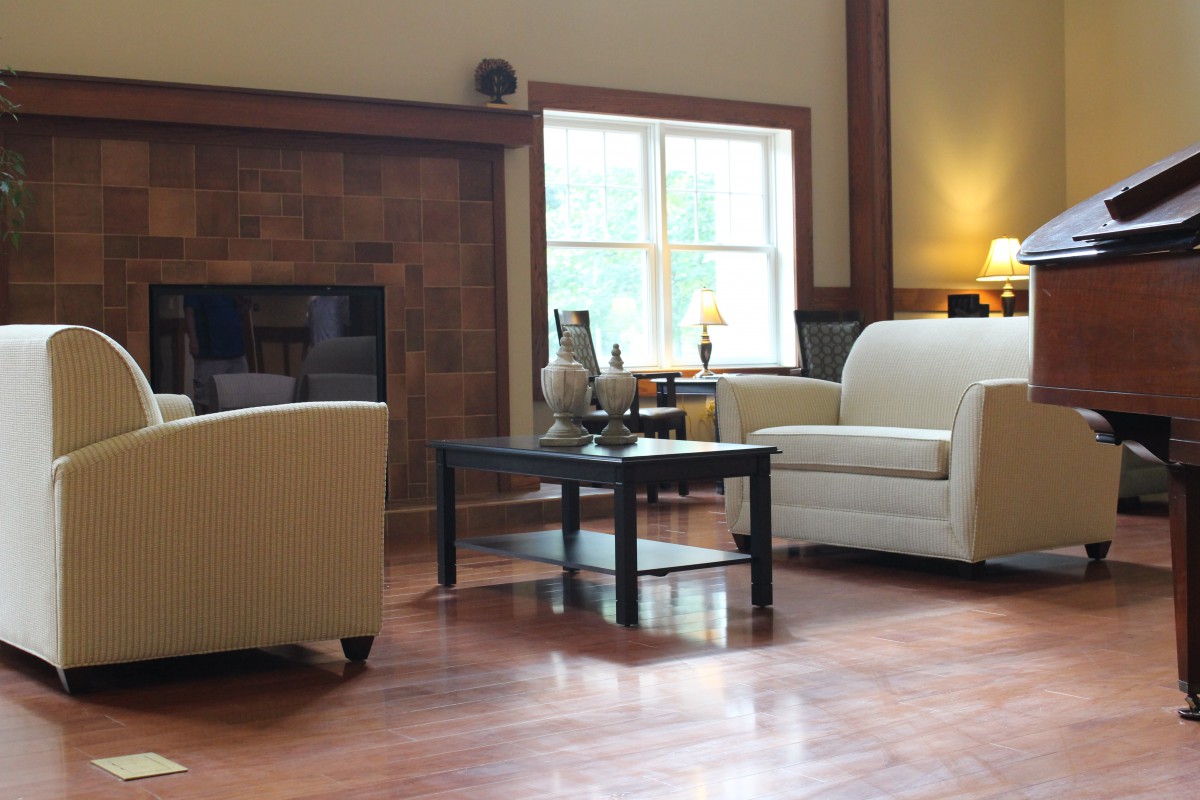 A cozy living room with a sofa, armchair, and coffee table, featuring a fireplace and hardwood flooring.