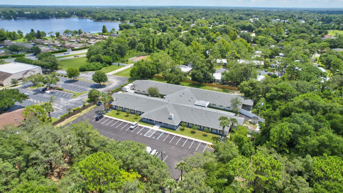 Aerial view of a building complex surrounded by lush greenery and a parking lot.