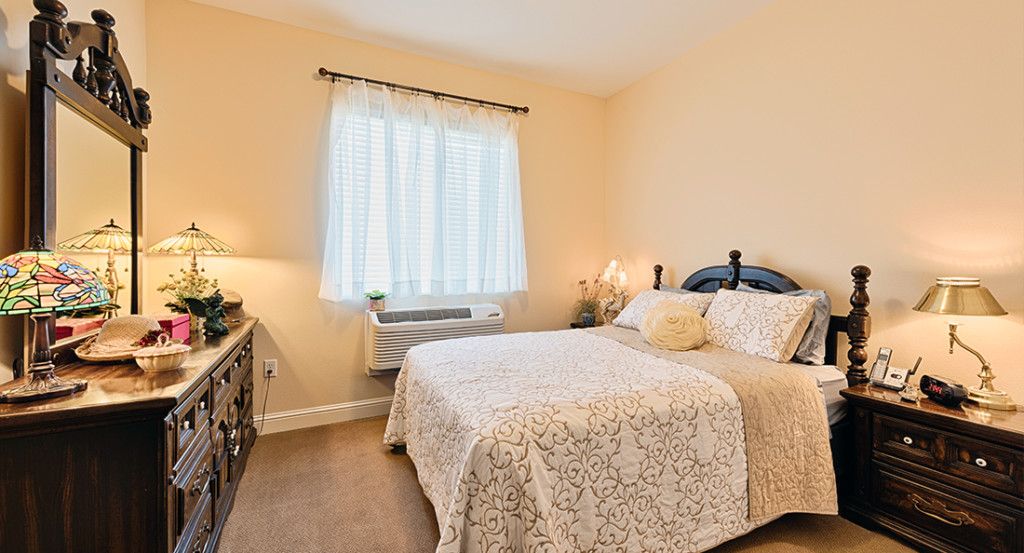 A cozy bedroom with a neatly made bed, soft lighting, and a window letting in natural light.