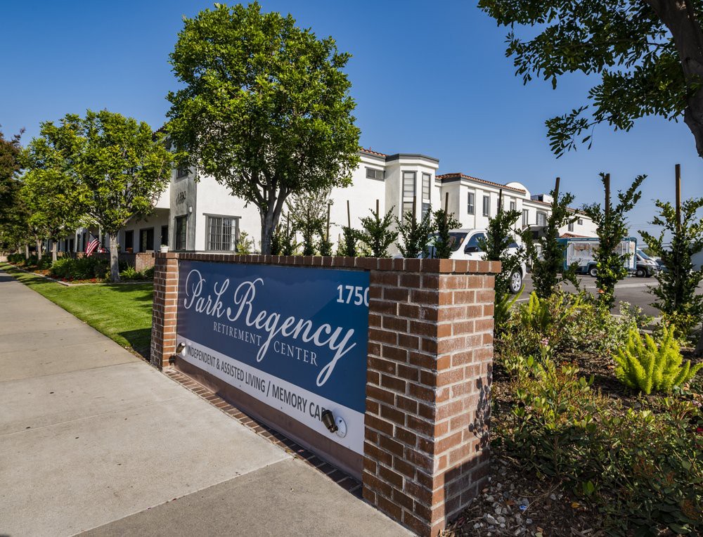 The image shows a hotel entrance with a sign and well-maintained landscaping.