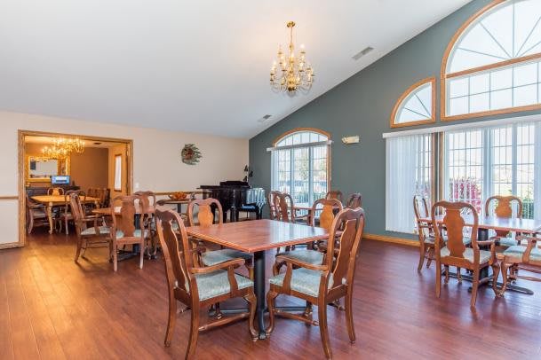 A spacious dining room featuring multiple tables and chairs, a chandelier, hardwood flooring, large windows, and a piano in the corner.