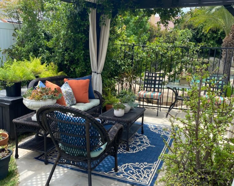 A cozy outdoor patio with comfortable seating, vibrant cushions, and lush greenery.