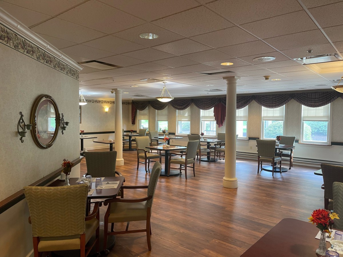 A cozy dining area with neatly arranged tables and chairs, featuring large windows and elegant curtains.