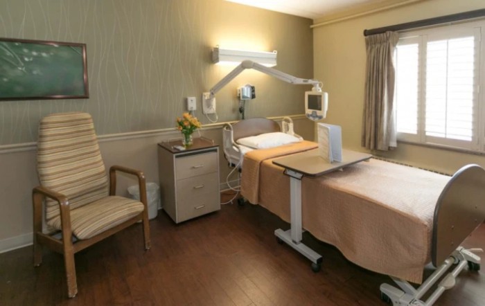 A well-equipped hospital room with a bed, medical equipment, and a chair.