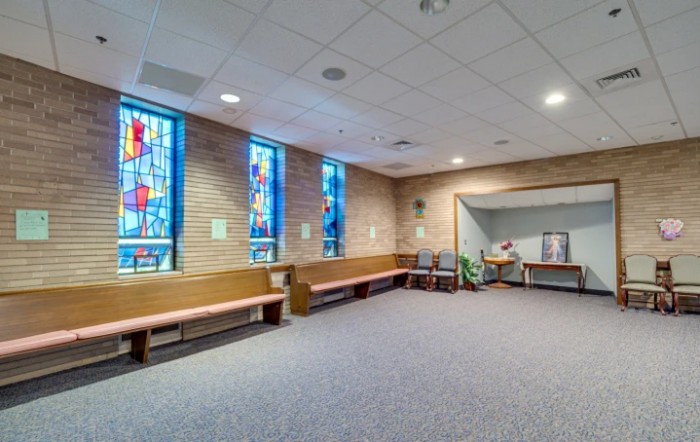 A small chapel room with stained glass windows and wooden benches.
