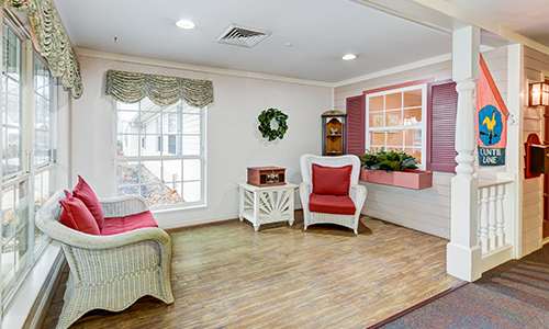 A cozy living room with wicker furniture and red cushions, featuring a large window and decorative pieces.