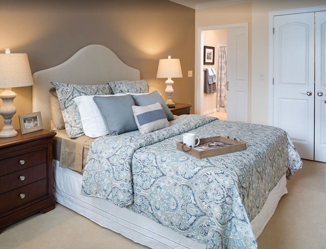 A cozy and elegantly designed bedroom with a neatly made bed, decorative pillows, a nightstand, and a lamp.