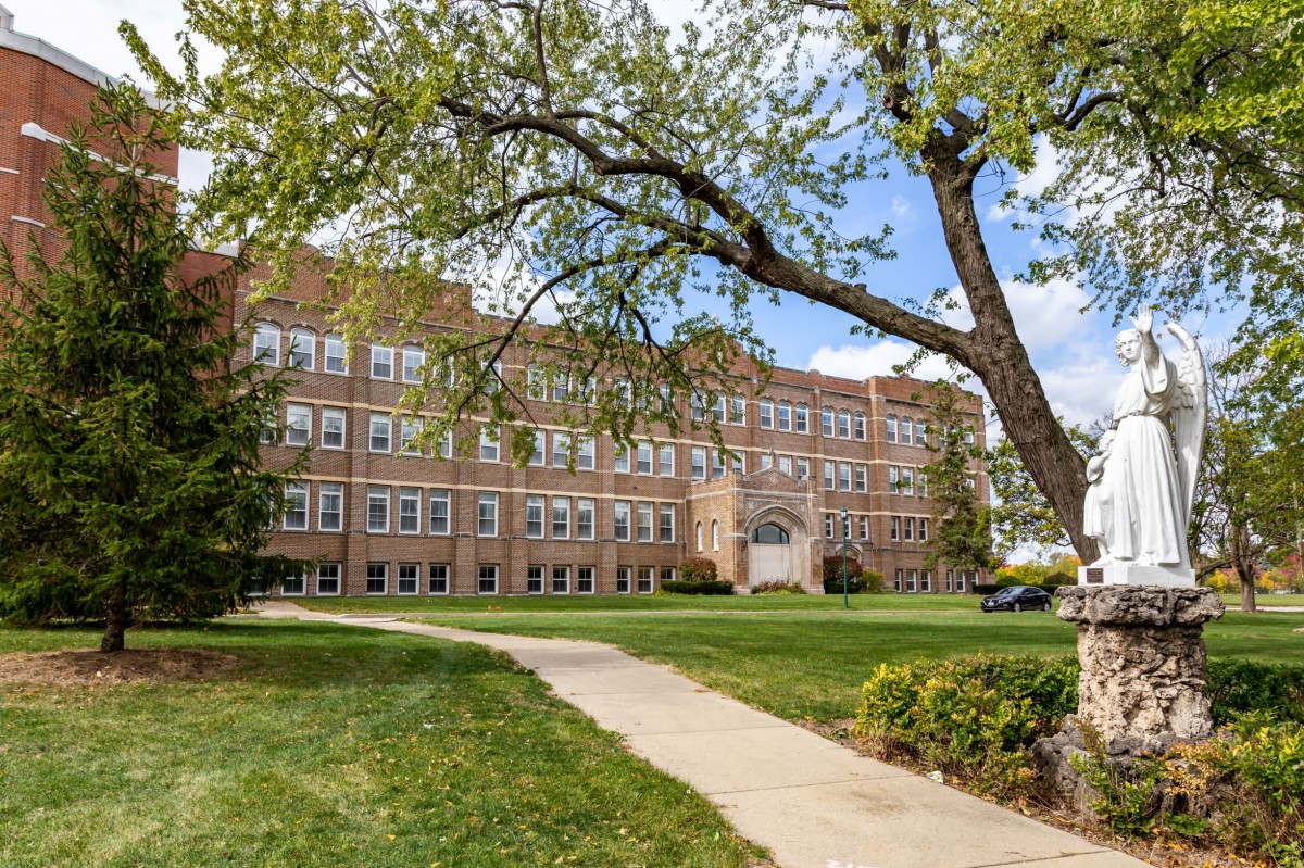 A large brick school building with a tree and well-maintained lawn in the foreground.