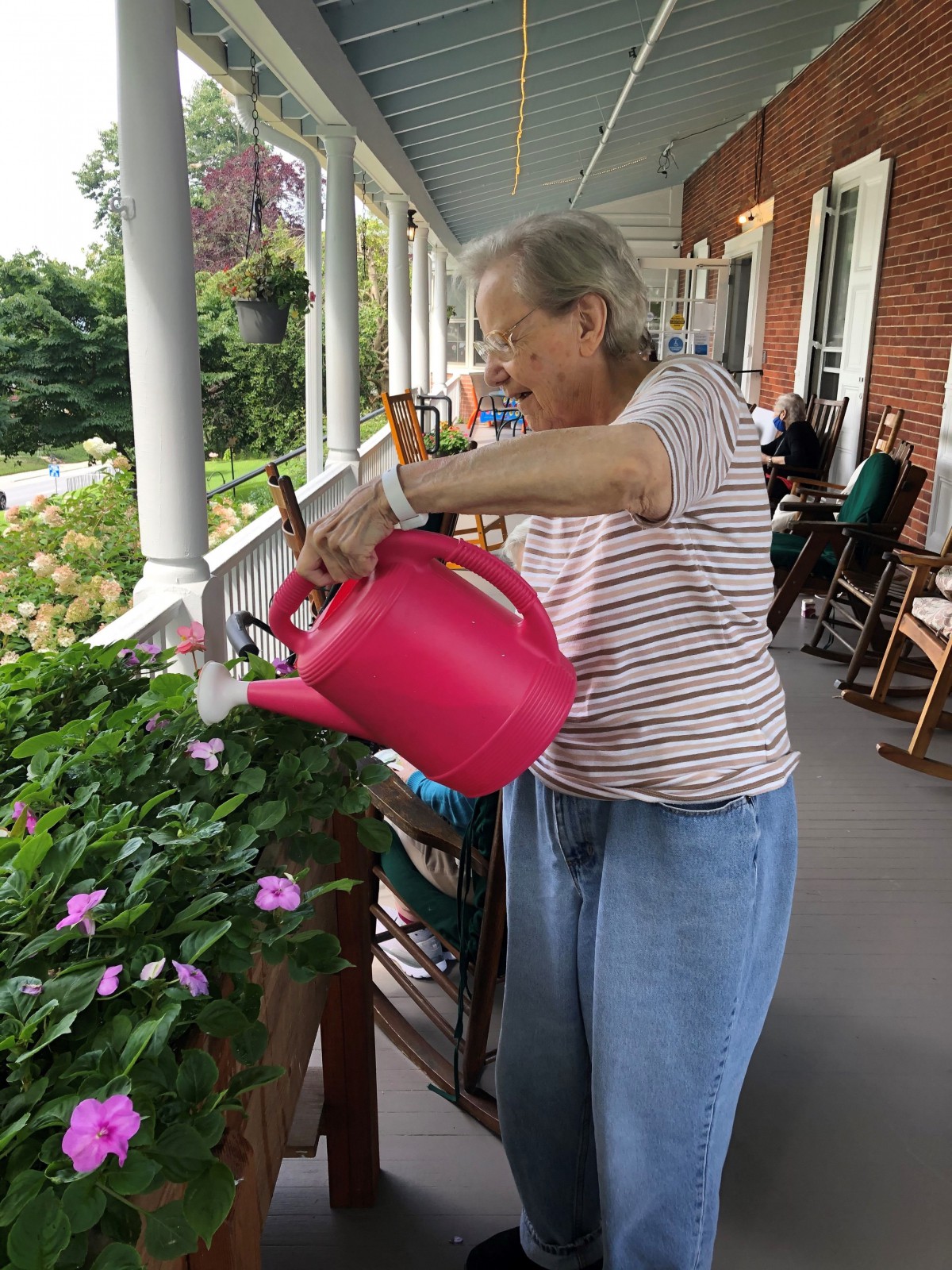 A person waters plants with a pink watering can on a porch.