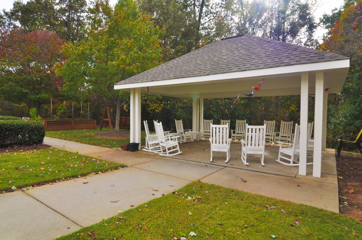 A peaceful outdoor gazebo with white rocking chairs surrounded by nature.
