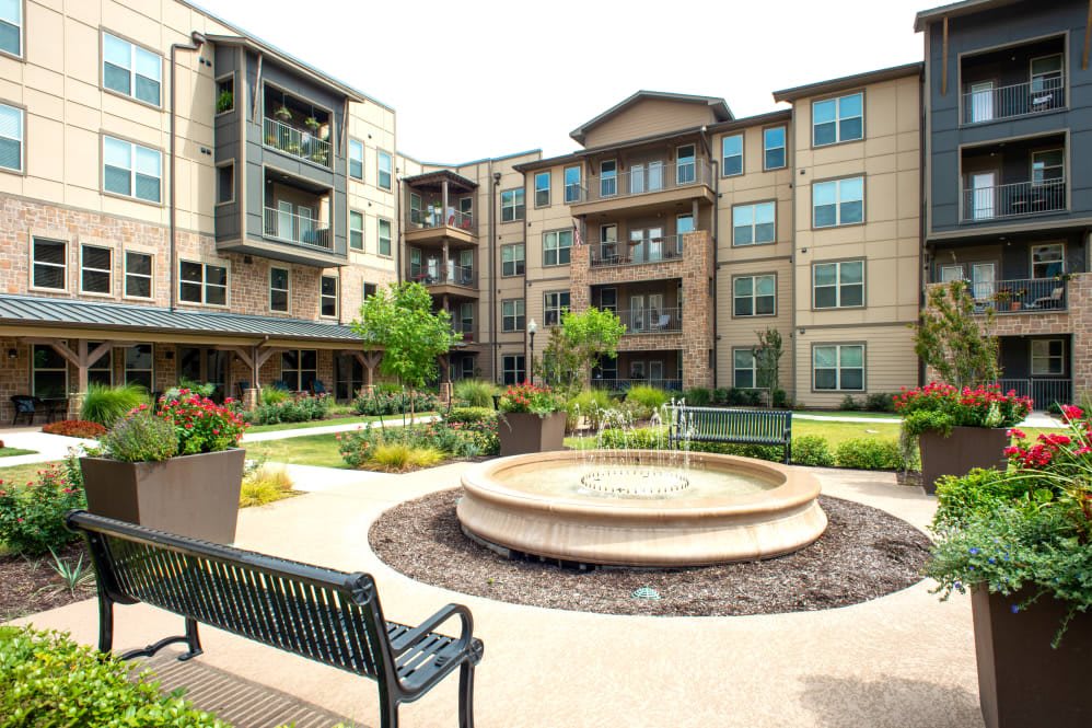 A modern apartment complex featuring a central courtyard with a fountain and outdoor seating.