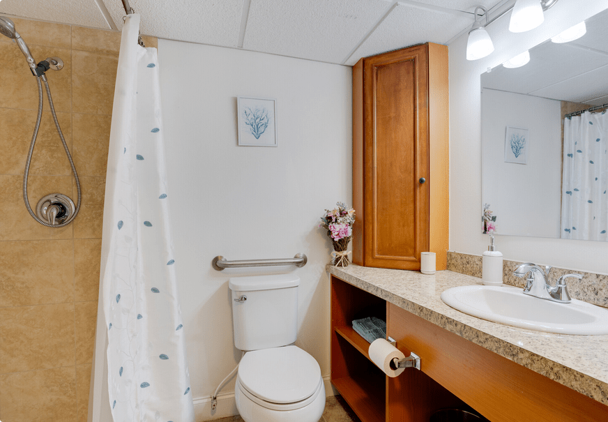 A clean and organized bathroom with a toilet, sink, mirror, and shower area.