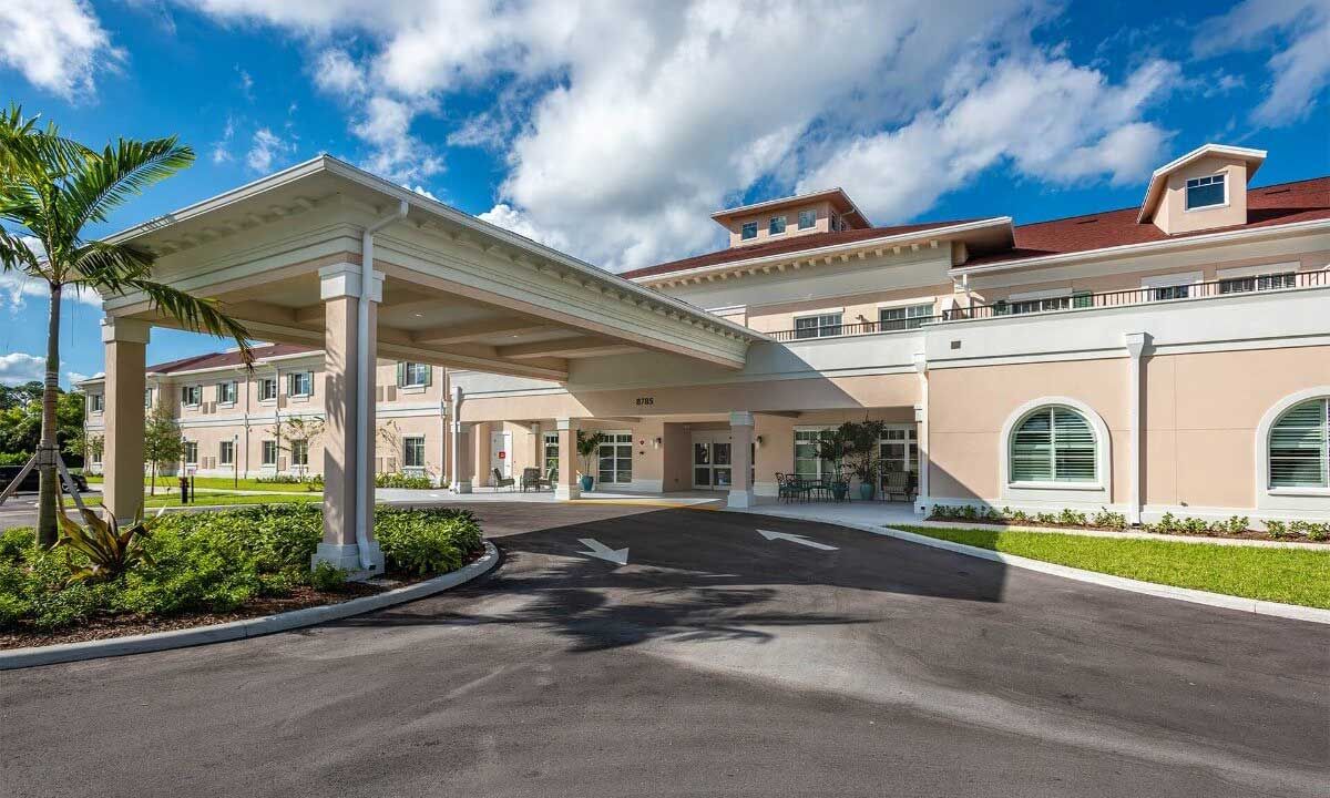 A modern building with a covered entrance and spacious driveway under a partly cloudy sky.