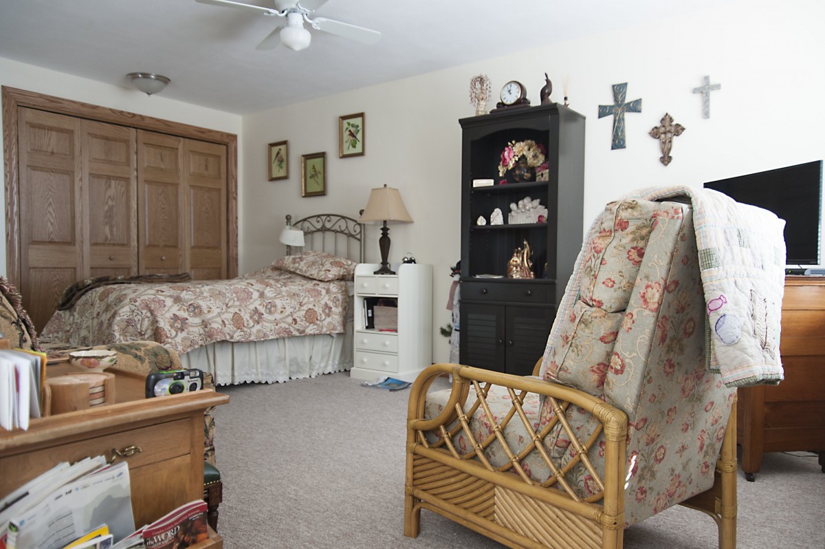 A cozy bedroom with a bed, bookshelf, and various decorative items including crosses on the wall.
