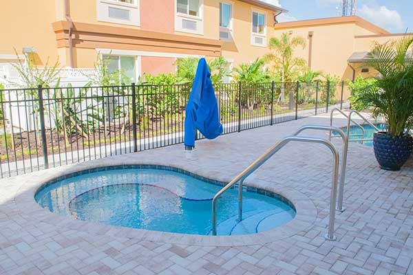 A cozy outdoor jacuzzi with a paved deck, surrounded by a secure fence and overlooked by an apartment building.