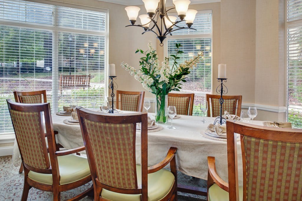 A well-lit dining room with a set table, elegant chairs, and a floral centerpiece.