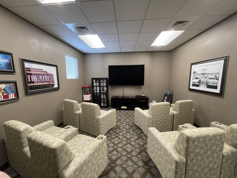 A cozy room with arranged chairs facing a television, decorated with wall art and carpet flooring.