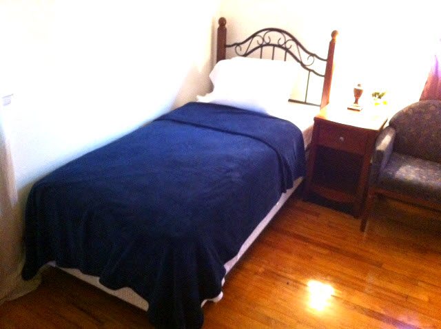 A minimalist bedroom featuring a single bed with a blue blanket and a wooden nightstand.