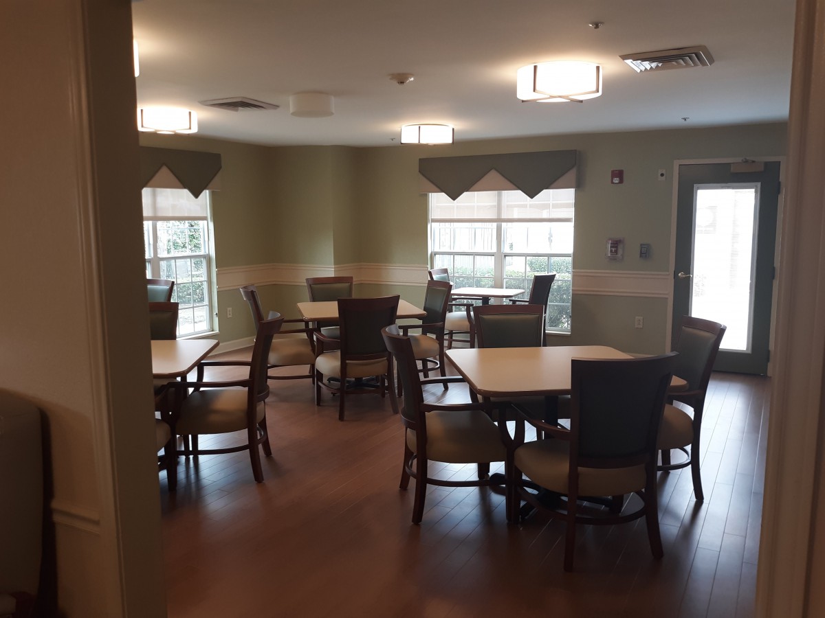 A dining area with several tables and chairs, featuring large windows and overhead lighting.