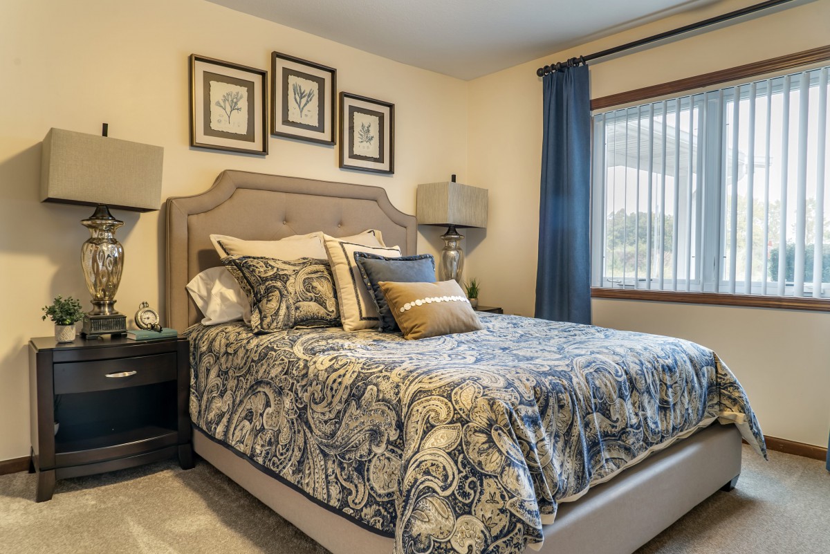 A cozy bedroom with elegant bedding, artwork on the wall, and a window with blue curtains.