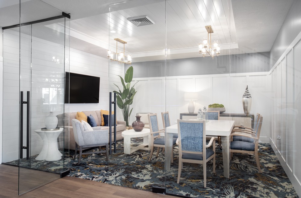 A modern conference room with glass walls, featuring a dining-style table and elegant chandeliers.