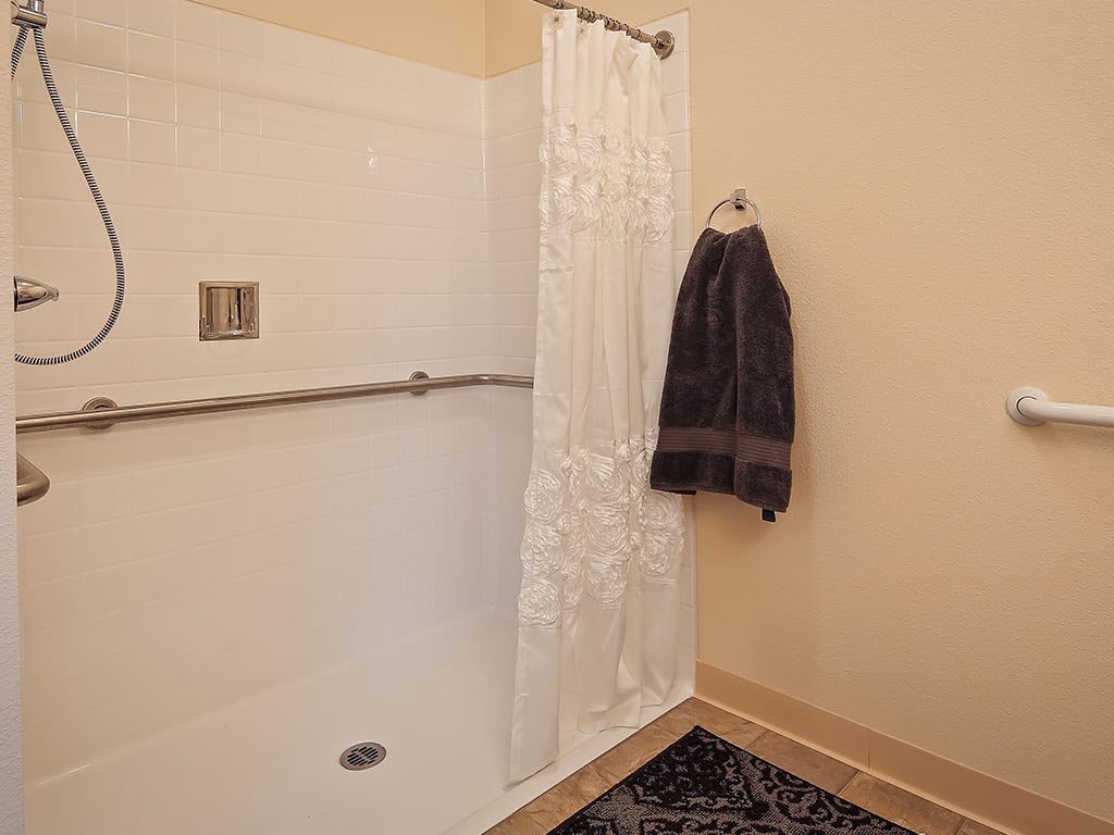 A bathroom with a shower area enclosed by a white curtain and a towel hanging on the wall.